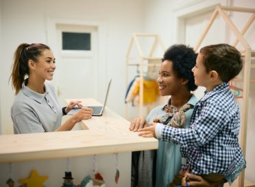 Happy black mother and her son talking to a teacher at reception desk at daycare.